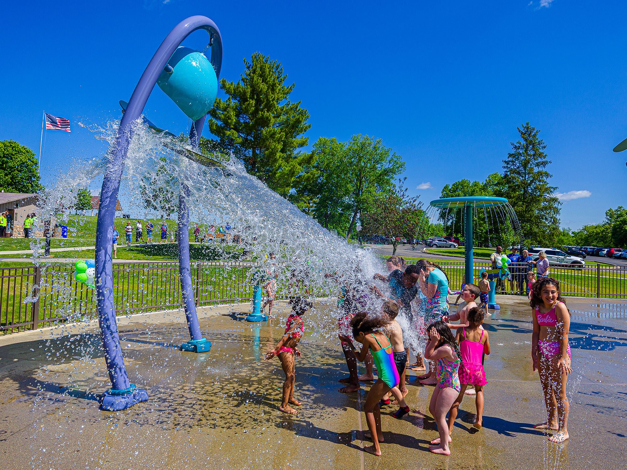 Kids gathered under tipping water bucket at splash pad