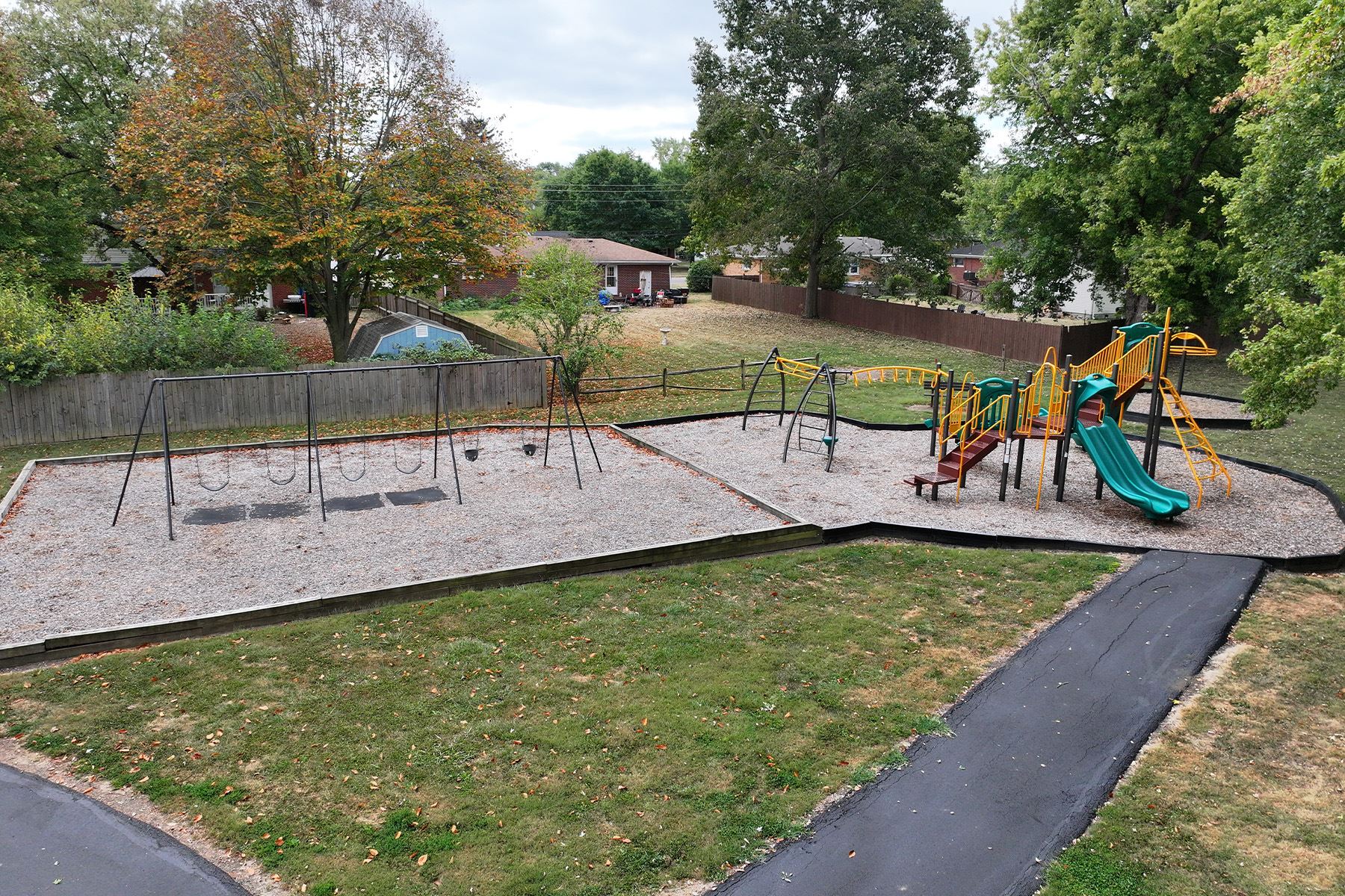 Playground with swings and climbing structures surrounded by trees.